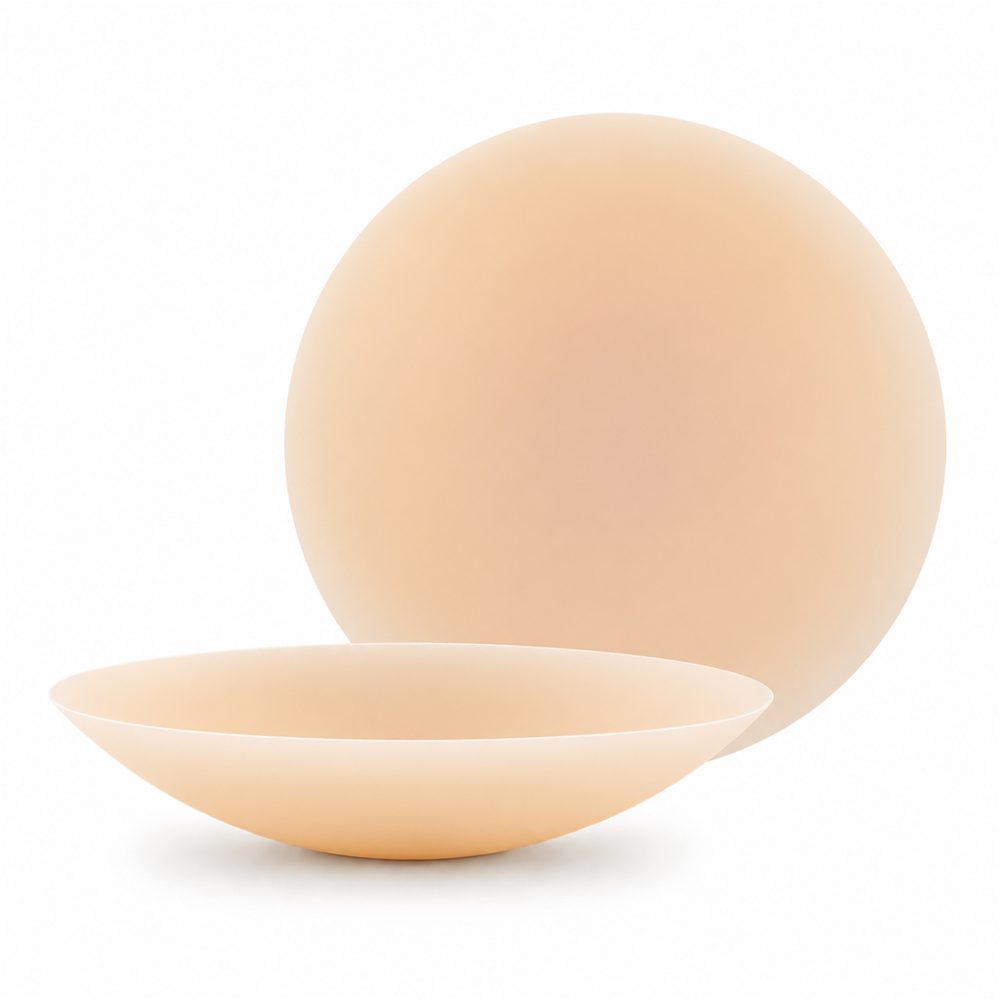 A pair of OMVY nipple covers in Nude, one seen from the side to show the tapered edge